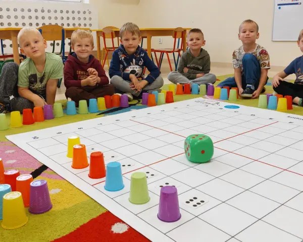 Dzieci uczą się kodowania dla przedszkolaków, bawiąc się kolorowymi kubeczkami i planszą z kostką.