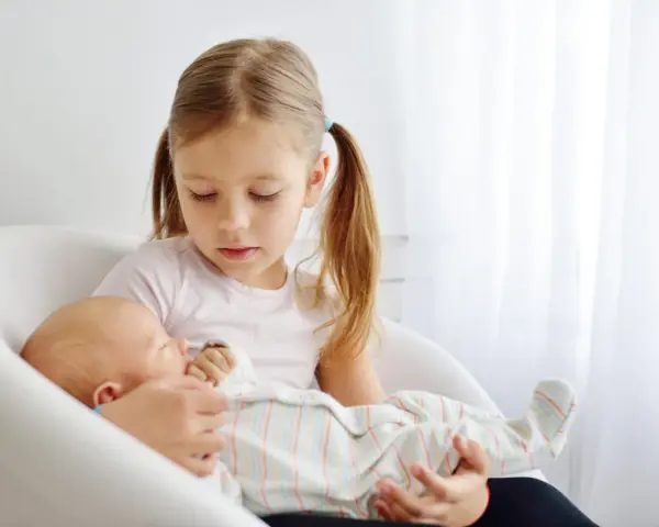 Starsza siostra delikatnie trzyma noworodka, ucząc się jak przygotować dziecko na rodzeństwo.