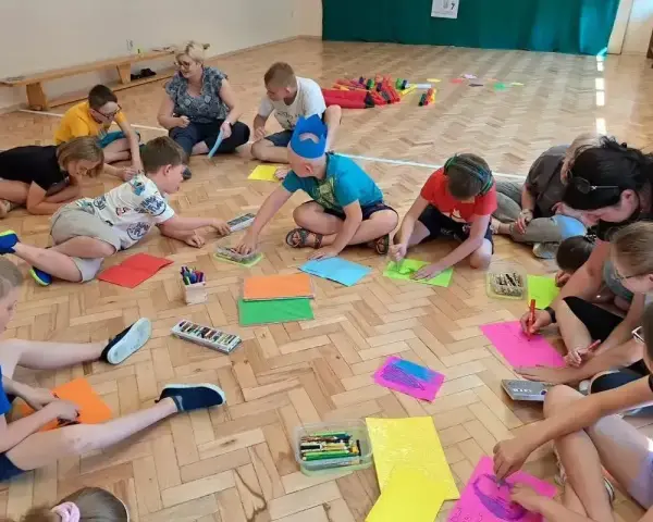 Wesołe zabawy w kole przedszkole. Dzieci siedzą na podłodze i rysują kolorowymi kredkami.