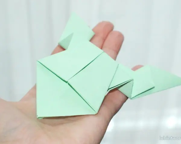 Zielona żaba z papieru, złożona techniką origami, spoczywa na dłoni.