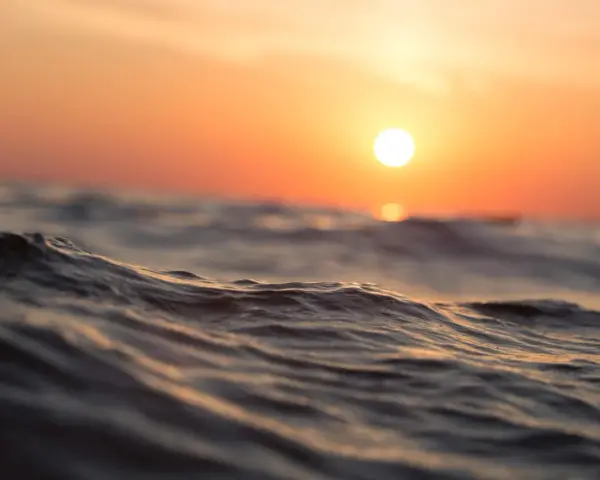 Piękne fale na morzu podczas zachodu słońca, jak z rysunku dla dzieci. Słońce maluje niebo na pomarańczowo.
