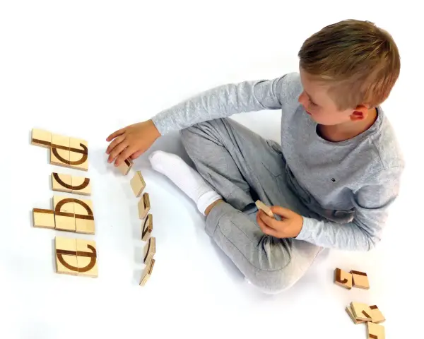 Chłopiec układa drewniane klocki z literami, ćwicząc czytanie klasa 1. Litery tworzą słowo "abcd".