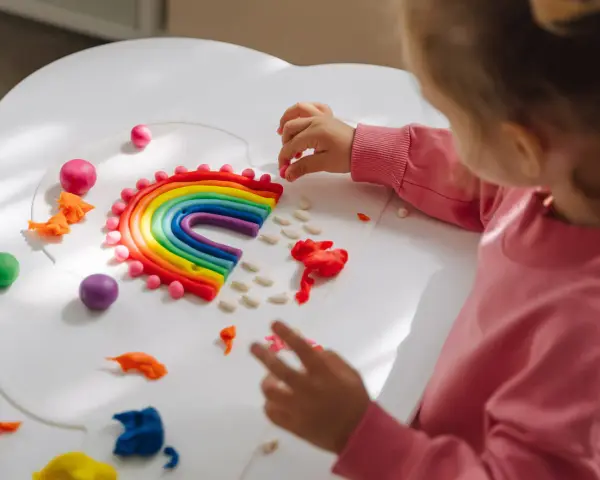 Dziecko tworzy tęczę z plasteliny, rozwiązując kreatywne wyzwania dla dzieci w domu. Kolorowa zabawa rozwija wyobraźnię.