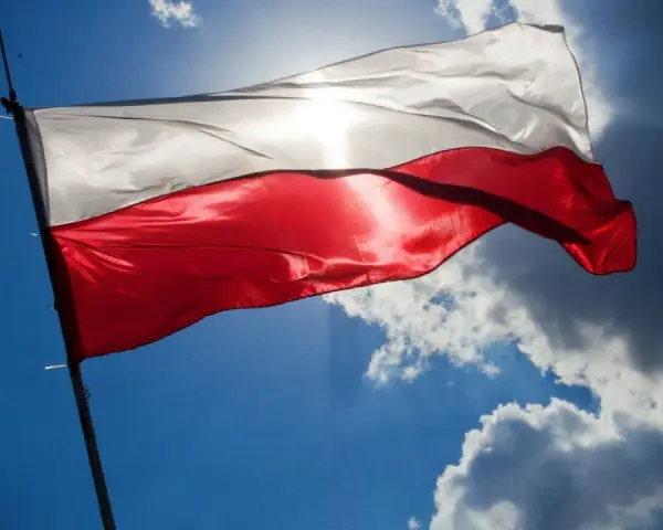 Biało-czerwona flaga powiewa na tle błękitnego nieba z chmurami. Wiatr rozwiewa ją, przypominając o pięknych cytatach o ojczyźnie.