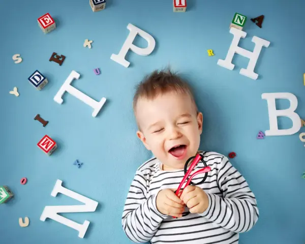Uśmiechnięte dziecko z zabawkami-literkami wokół. Słyszy "mama" i cieszy się.