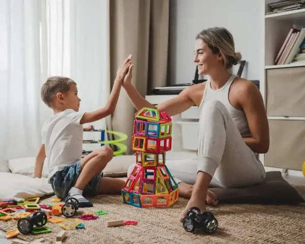 Mama i syn świętują sukces budowli z klocków magnetycznych. To świetne kreatywne zabawy dla 8 latka, rozwijające wyobraźnię i zdolności manualne.