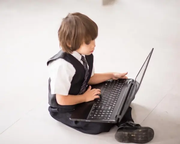 Elegancki chłopiec w garniturze odkrywa świat w internecie, siedząc na podłodze z laptopem.