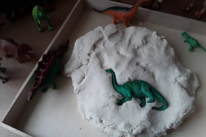 Zabawy z masą plastyczną i figurkami dinozaurów to świetne pomysły na dzień dinozaura. Dzieci mogą tworzyć prehistoryczne krajobrazy.
