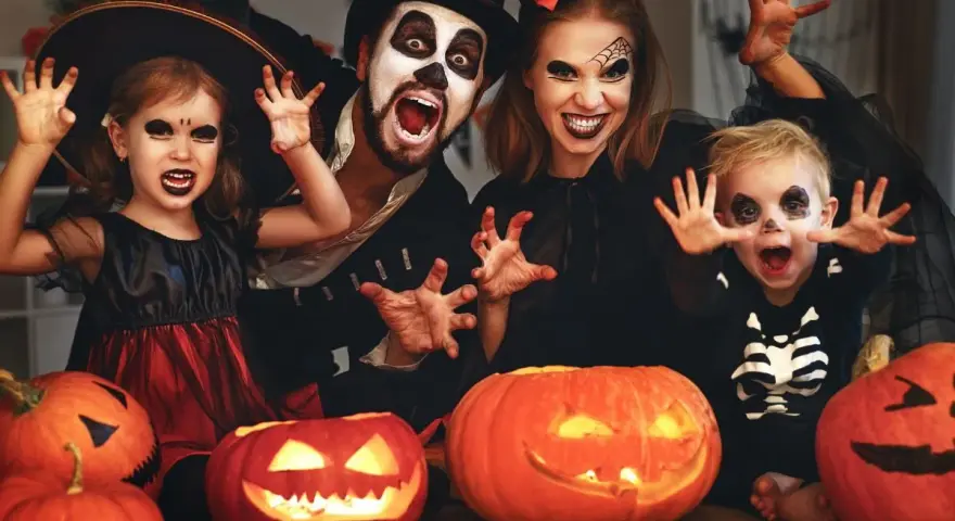 Rodzina w strojach na Halloween, z dyniami i pajęczyną w tle. Idealne inspiracje na halloween karty pracy dla dzieci.