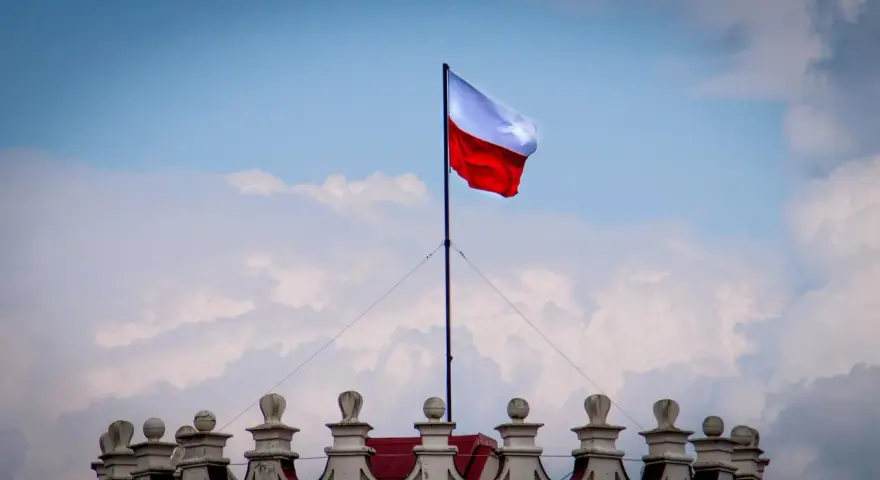 Biało-czerwona flaga powiewa na maszcie nad zabytkowym budynkiem. Wiatr rozwiewa ją, jakby niosła słowa o Polsce.