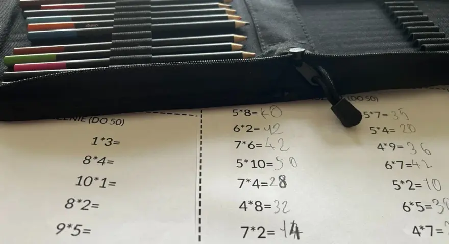 Karta pracy z tabliczką mnożenia do 100. Obok leżą kolorowe kredki w etui.