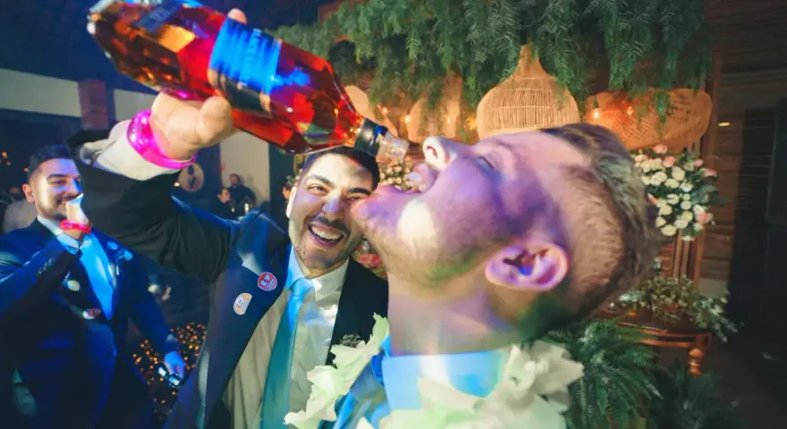 Szampańskie zabawy na imprezie! Mężczyzna nalewa alkohol prosto do ust przyjaciela, obaj uśmiechnięci i pełni radości.