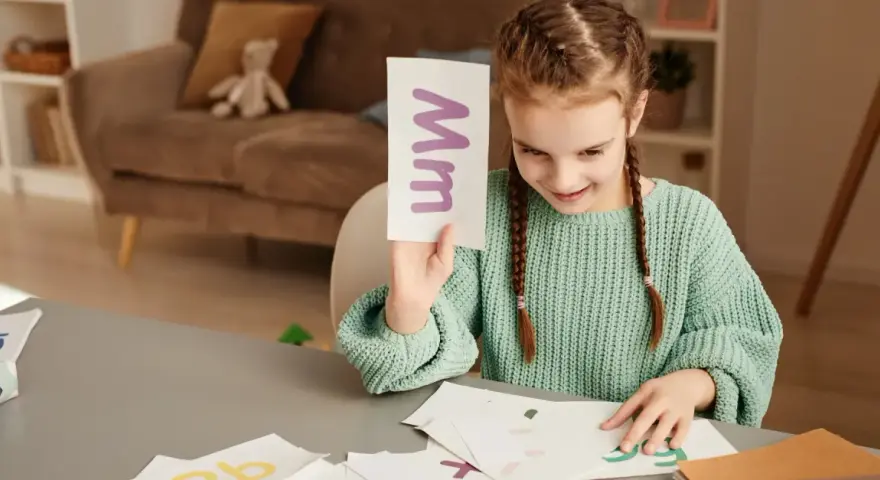 Dziewczynka uczy się literki "M". Na karcie widnieje duża i mała litera "m". To świetna zabawa z wyrazami na m dla dzieci.
