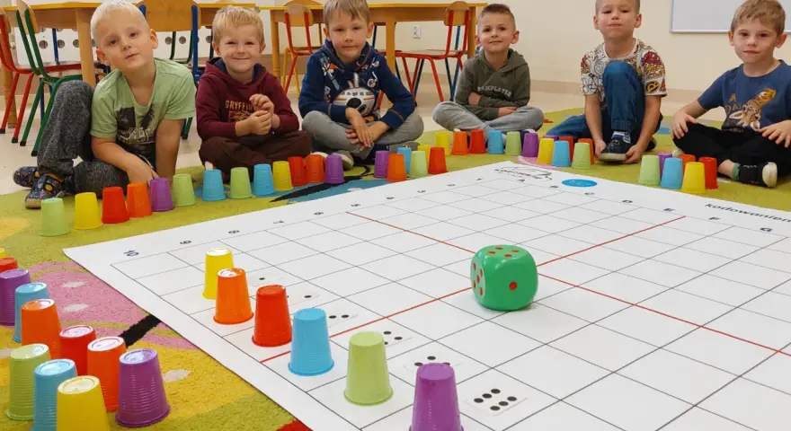 Dzieci uczą się kodowania dla przedszkolaków, bawiąc się kolorowymi kubeczkami i planszą z kostką.