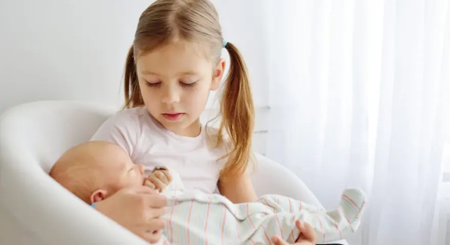 Starsza siostra delikatnie trzyma noworodka, ucząc się jak przygotować dziecko na rodzeństwo.