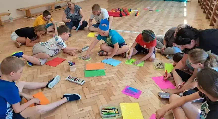 Wesołe zabawy w kole przedszkole. Dzieci siedzą na podłodze i rysują kolorowymi kredkami.