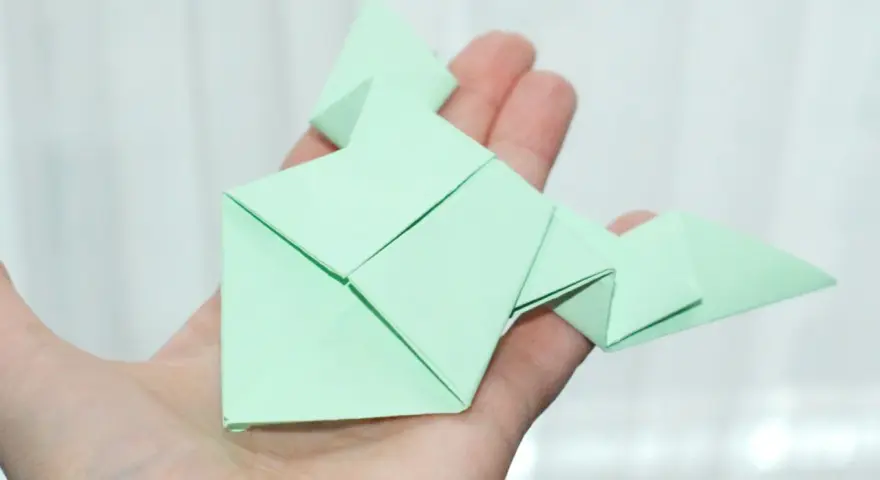 Zielona żaba z papieru, złożona techniką origami, spoczywa na dłoni.