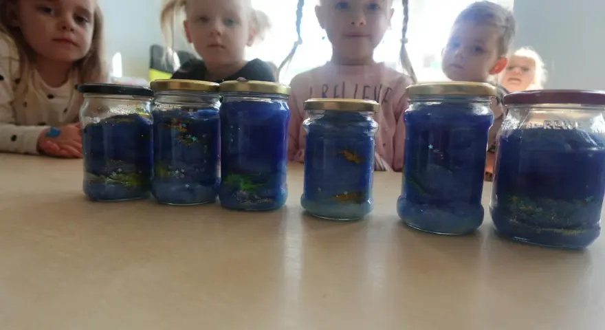 Dzieci tworzą galaktykę w słoiku, dodając brokat i niebieską masę.