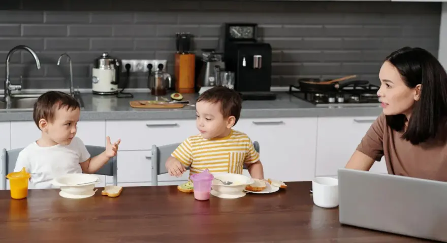 Mama słucha, jak dziecko zaczyna mówić pierwsze zdania, podczas wspólnego posiłku w kuchni.