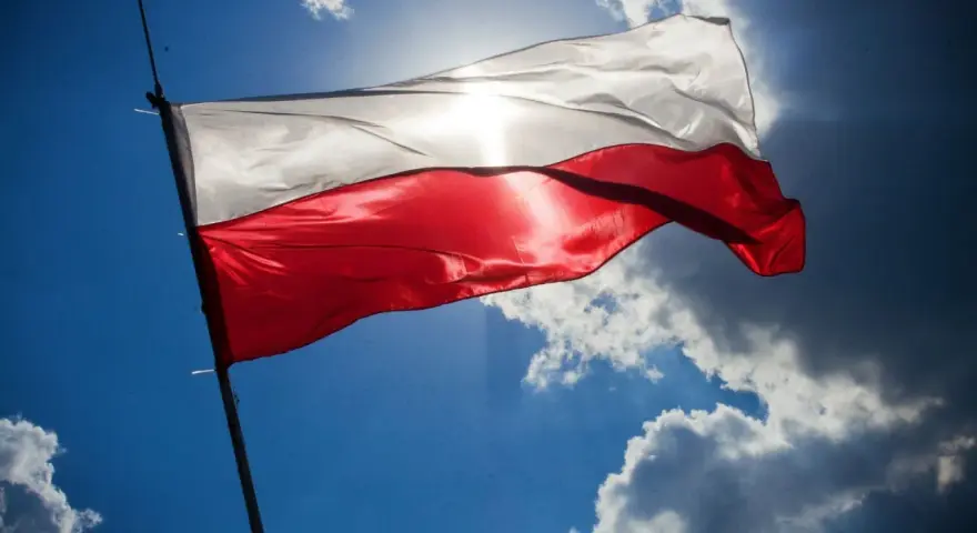 Biało-czerwona flaga powiewa na tle błękitnego nieba z chmurami. Wiatr rozwiewa ją, przypominając o pięknych cytatach o ojczyźnie.