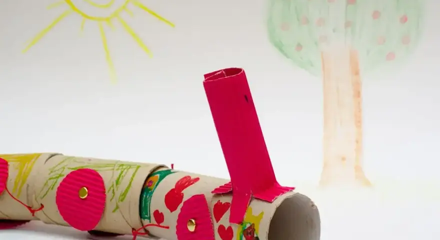 Kolorowy pociąg z rolek po papierze toaletowym, wykonany z rzeczy z recyklingu dla dzieci. W tle rysunek słońca i drzewa.