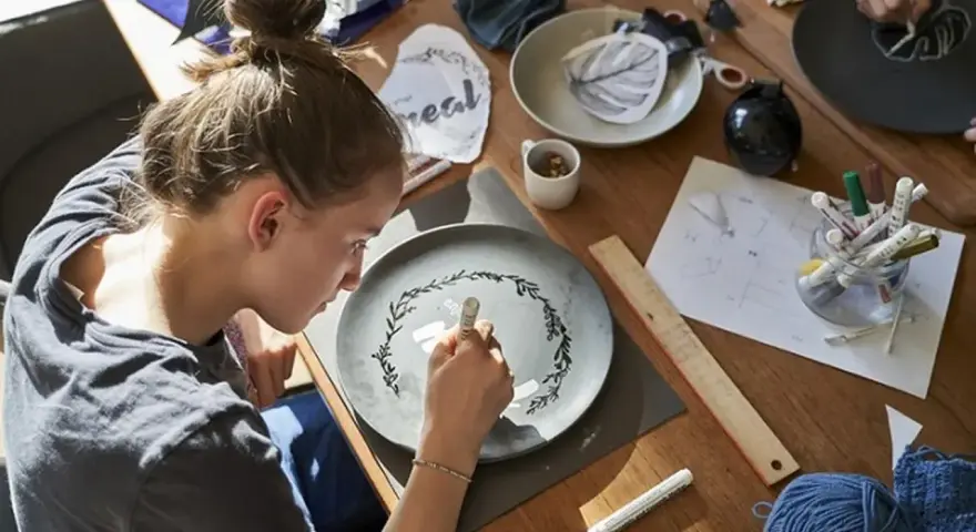 Dziewczyna maluje wzór na talerzu, tworząc własny przepis na masę porcelanową.