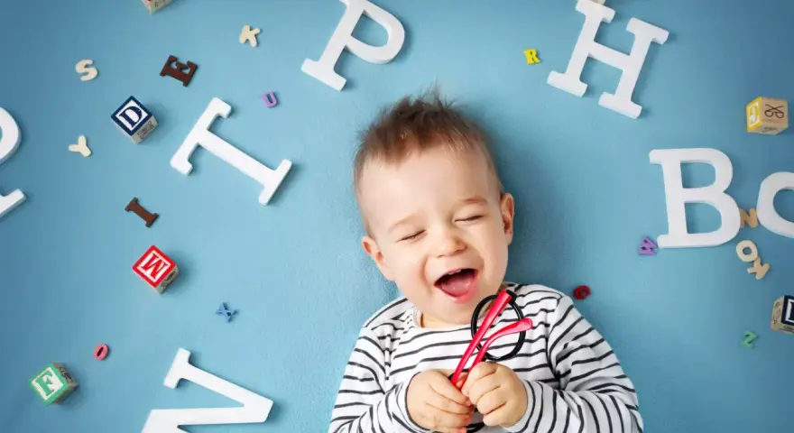 Uśmiechnięte dziecko z zabawkami-literkami wokół. Słyszy "mama" i cieszy się.