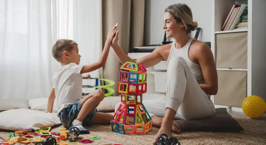 Mama i syn świętują sukces budowli z klocków magnetycznych. To świetne kreatywne zabawy dla 8 latka, rozwijające wyobraźnię i zdolności manualne.