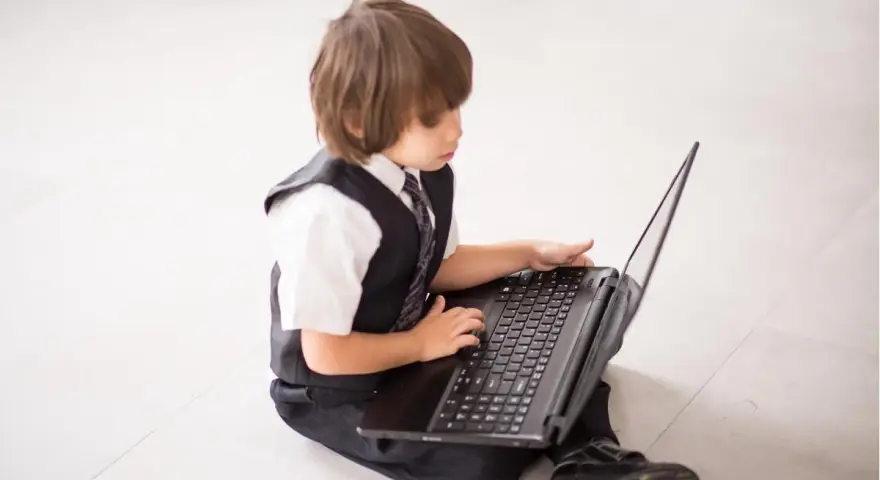 Elegancki chłopiec w garniturze odkrywa świat w internecie, siedząc na podłodze z laptopem.