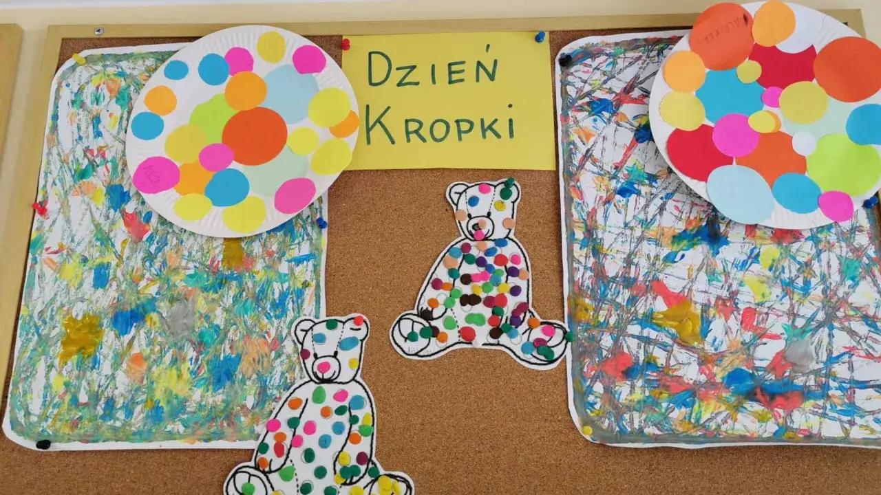 Kolorowe prace plastyczne na tablicy z okazji Dnia Kropki: misie w kropki i abstrakcyjne tła.