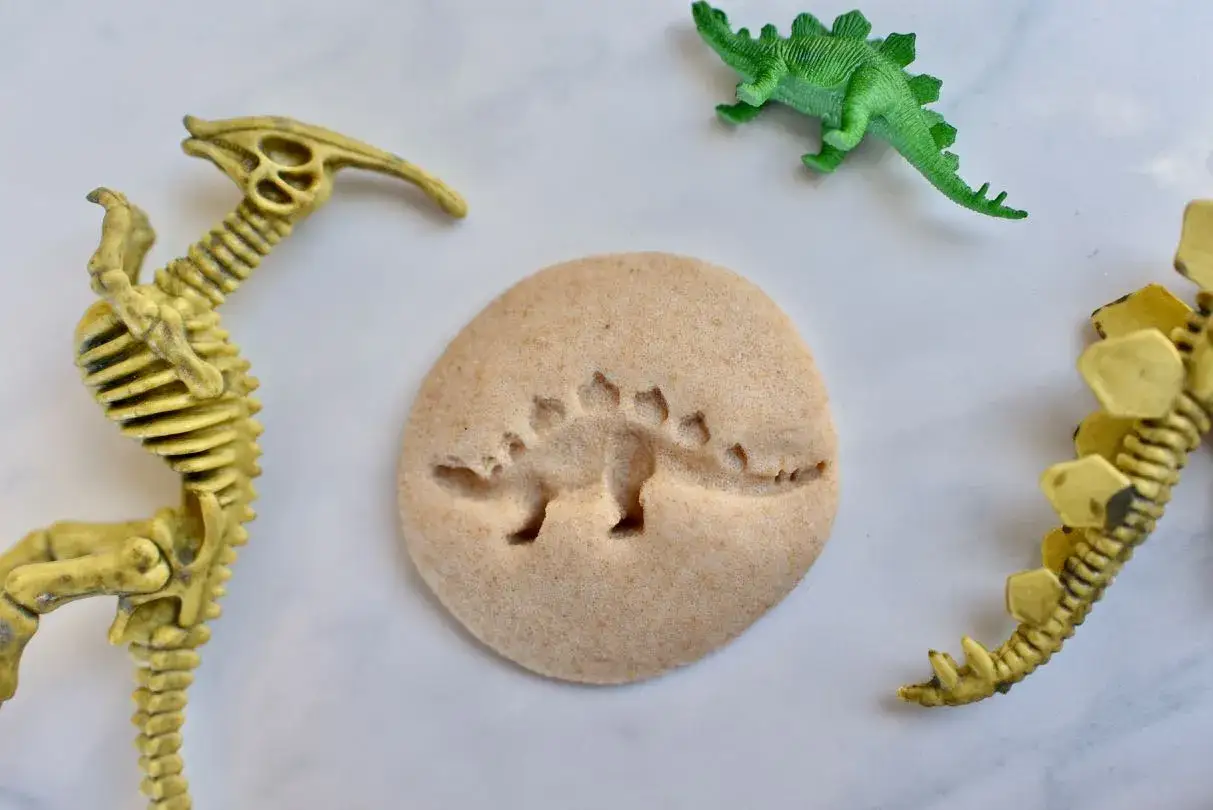 Szkielet dinozaura praca plastyczna: żółte szkielety i zielony dinozaur otaczają okrągły odcisk dinozaura.