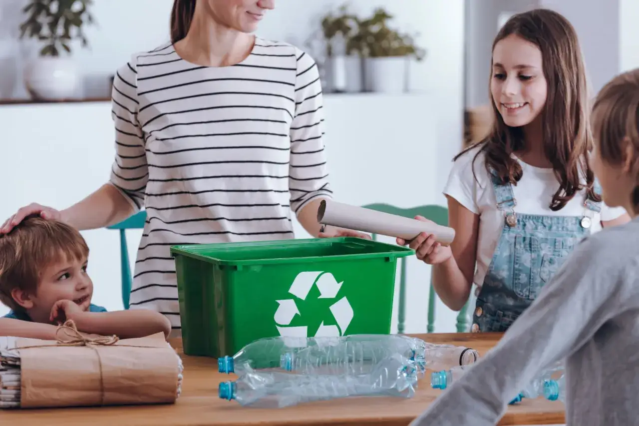 Rodzina uczy dzieci ekologii, segregując śmieci. Zielony pojemnik na odpady i plastikowe butelki na stole.
