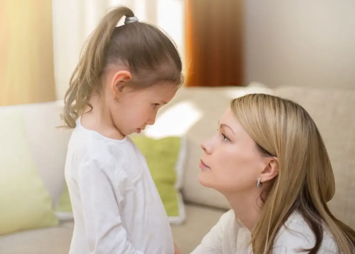 Mama rozmawia z córką, wspierając jej rozwój emocjonalny dziecka. Dziewczynka patrzy w dół, mama z troską w oczy.