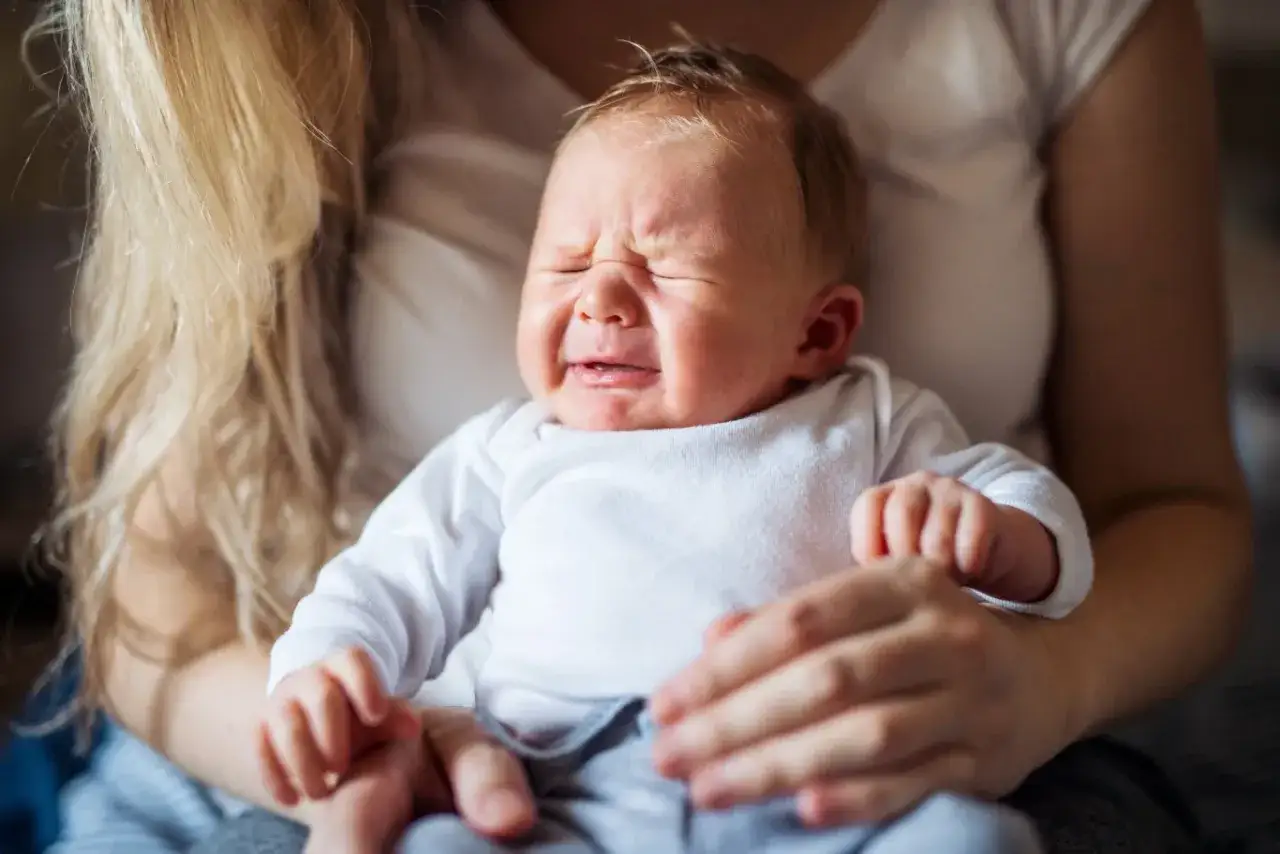 Płacz dziecka, które mama próbuje uspokoić. Delikatne dłonie otulają maluszka, szukając sposobu, jak uspokoić dziecko.