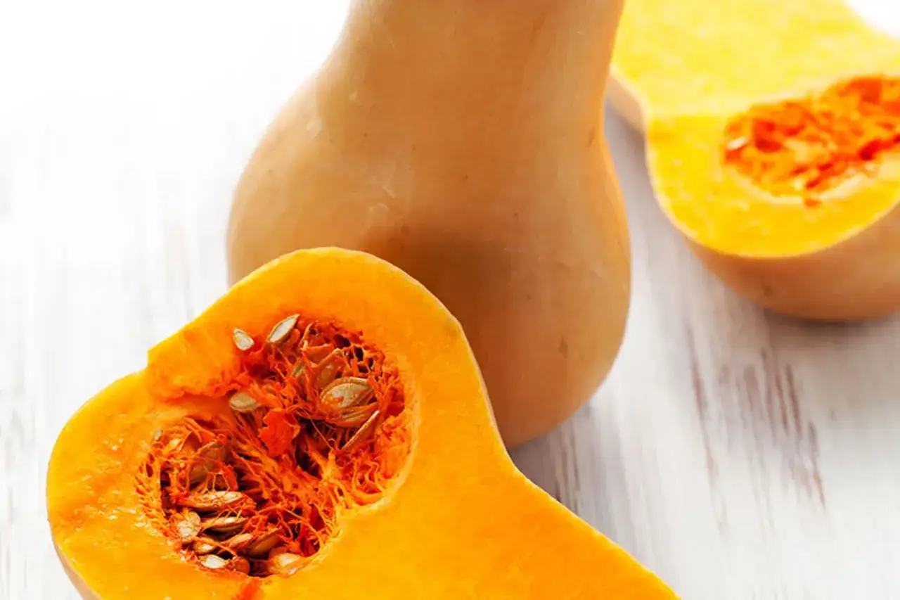 Ciekawostki o dyni: ta pomarańczowa dynia typu butternut, przekrojona na pół, odsłania swoje nasiona i miąższ.