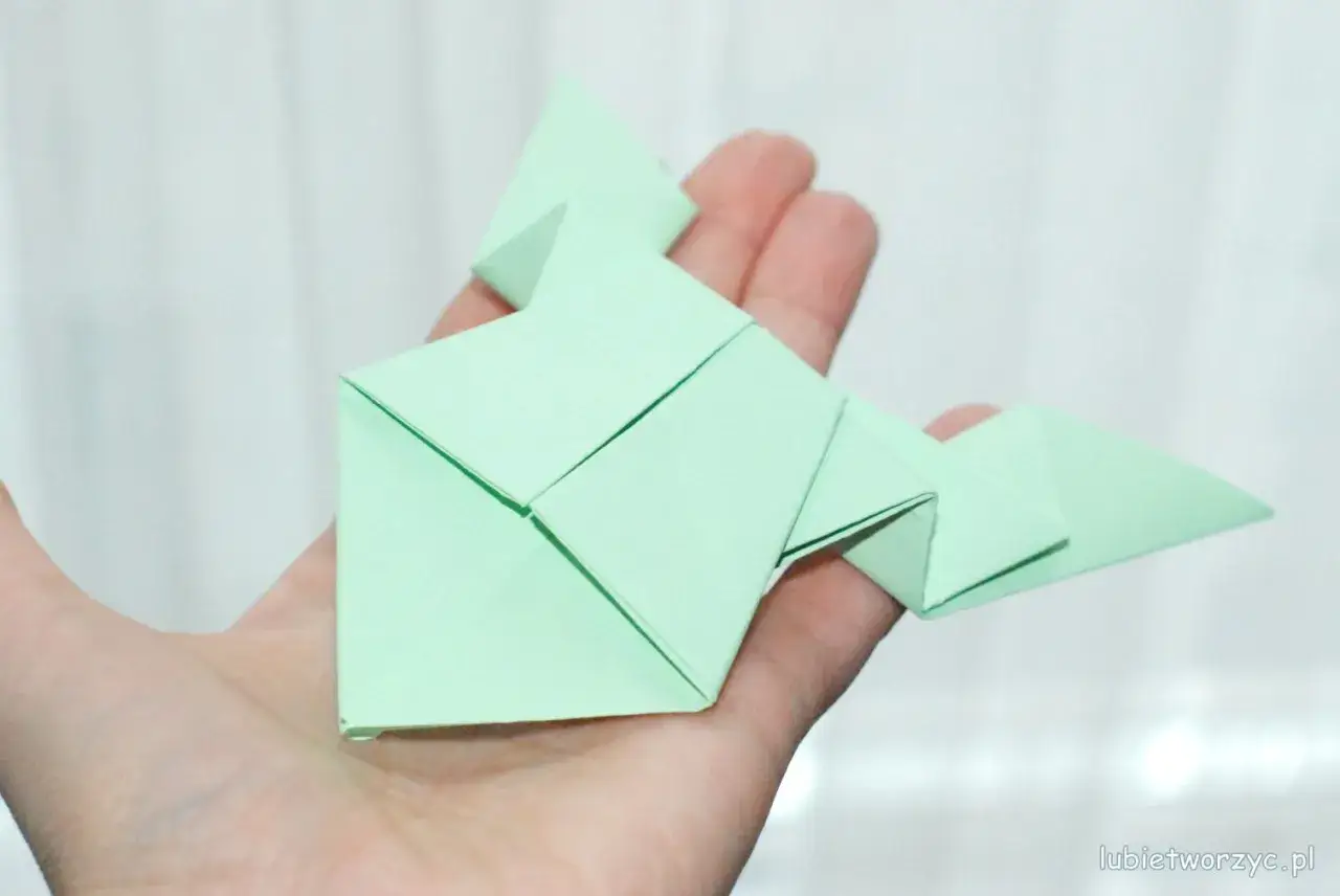 Zielona żaba z papieru, złożona techniką origami, spoczywa na dłoni.