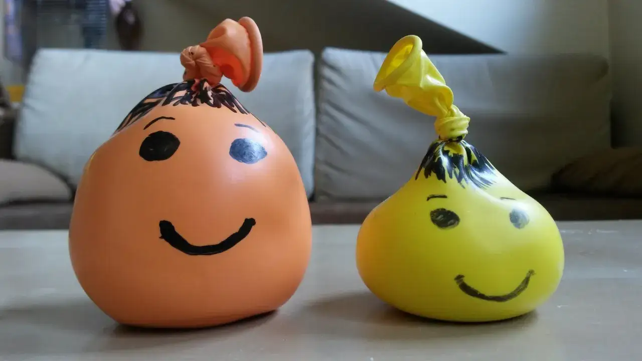 Dwa balony z namalowanymi buźkami, pomarańczowy i żółty, wyglądają jak gniotki zrobione z mąki i wody.