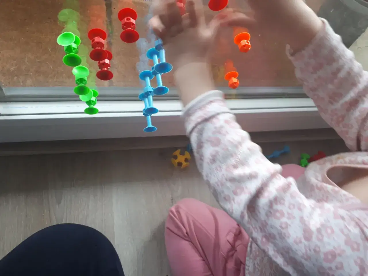 Roczne dziecko bawi się kolorowymi przyssawkami na oknie, rozwijając swoje zabawy sensoryczne.