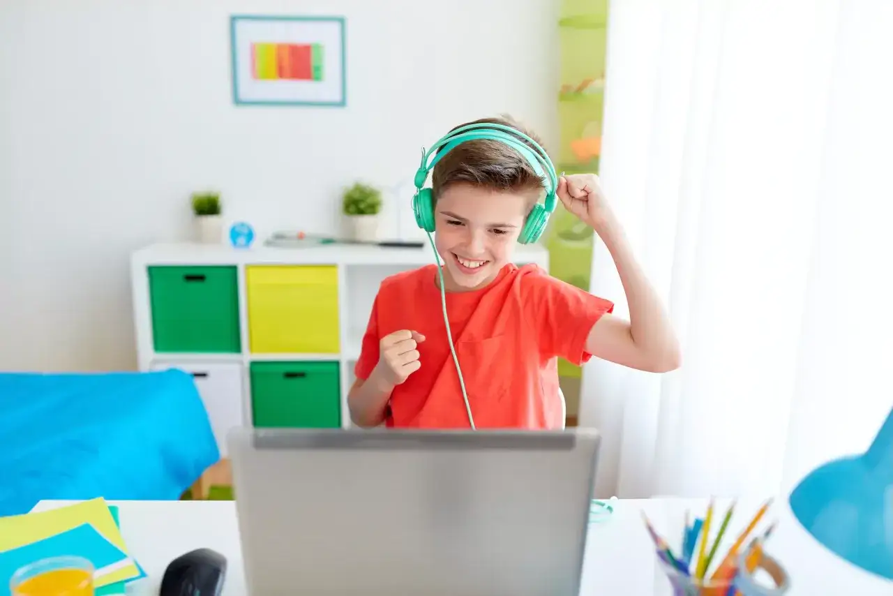 Chłopiec w słuchawkach cieszy się z sukcesu w grach edukacyjnych online.