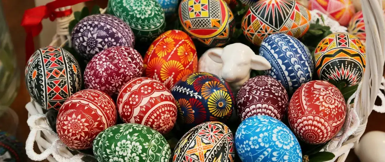 Wielkanocna prezentacja tradycji: kosz pełen barwnych, ręcznie zdobionych pisanek i ceramiczna figurka baranka.