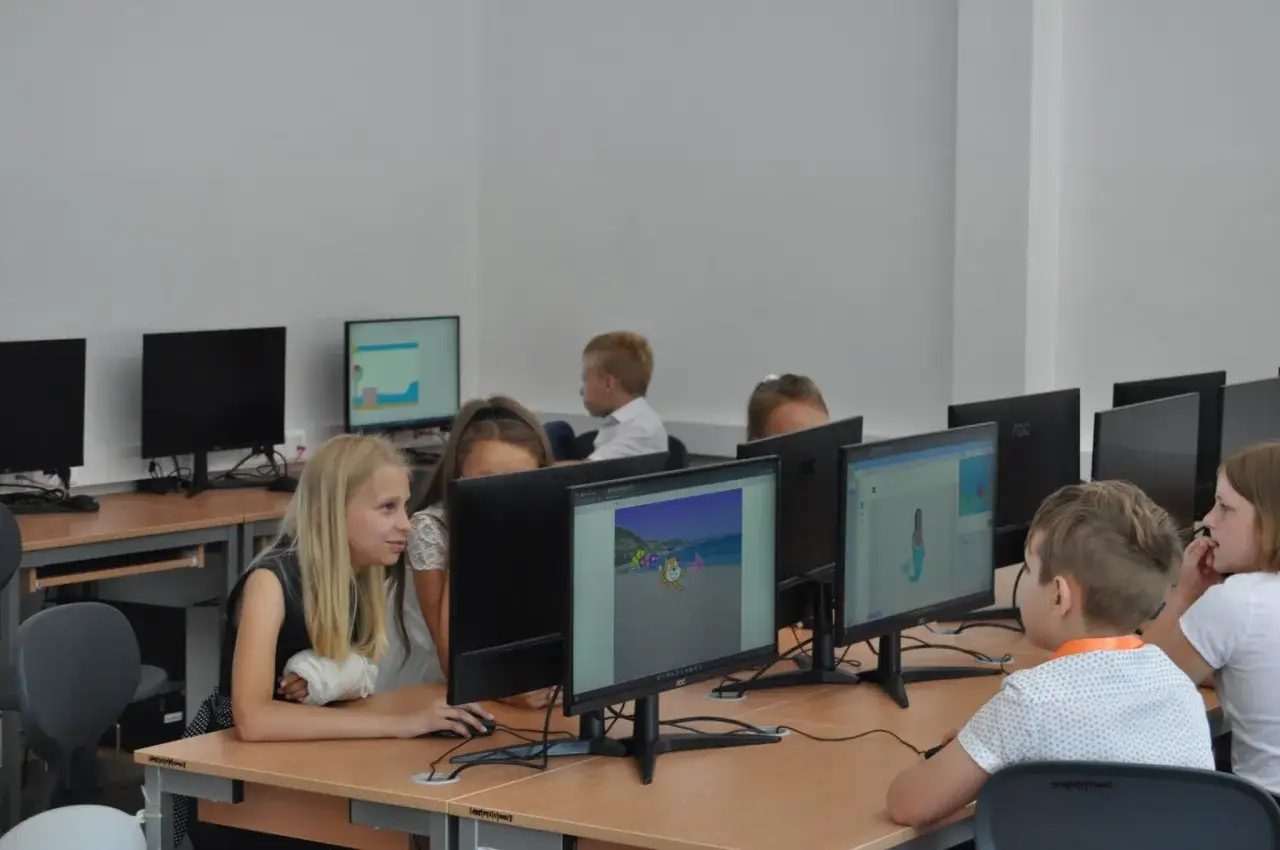 Uczniowie klasy 1 na lekcji informatyki tworzą projekty w Scratchu. Dzieci pracują przy komputerach, tworząc animacje i gry.